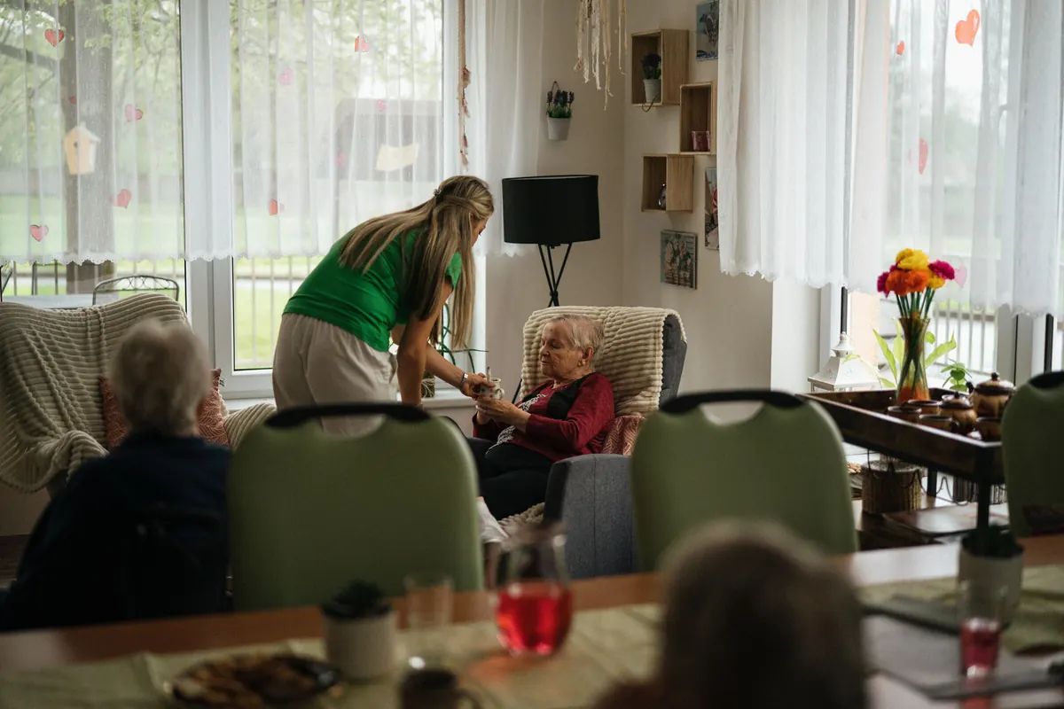 Caregiver serving tea to elderly residents in a nursing home common room