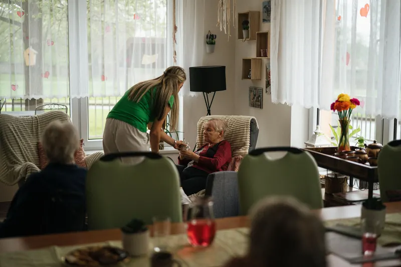 Caregiver serving tea to elderly residents in a nursing home common room