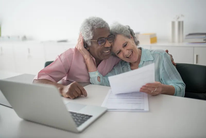 Senior couple reviewing paperwork and bills at a table with a laptop
